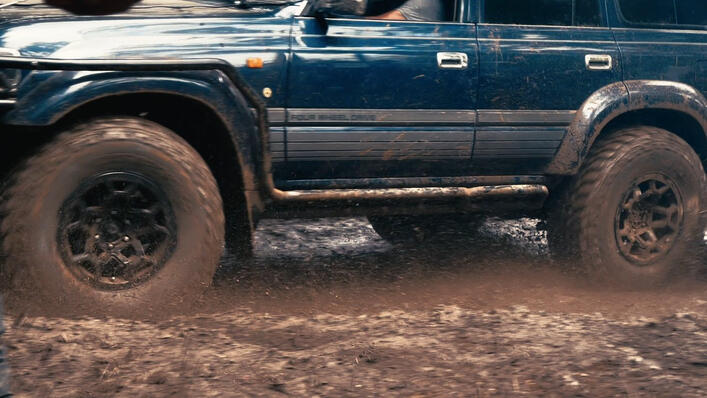 Modified Toyota Land Cruiser driving through deep mud during an off-road 4x4 adventure, splashing water across a challenging muddy trail. Modified Toyota Land Cruiser driving through deep mud during an off-road 4x4 adventure, splashing water across a challenging muddy trail.