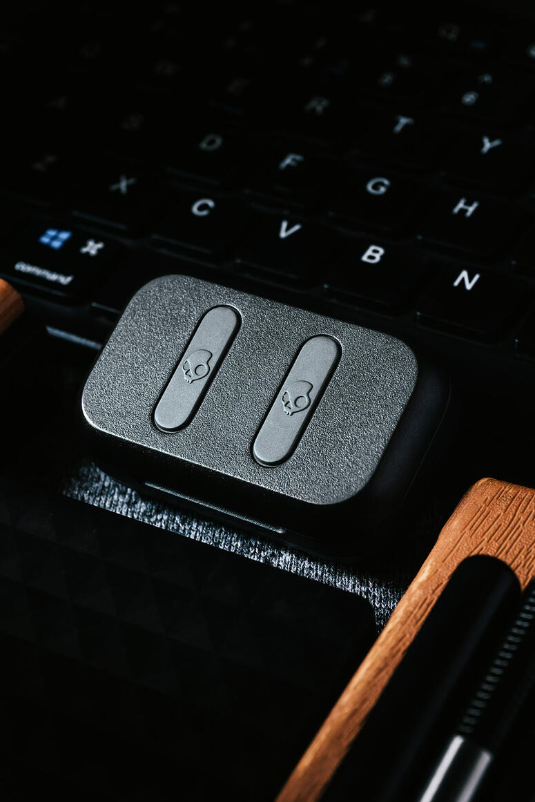 Close-up of a black device with two skull icons on buttons, placed on a laptop keyboard with visible keys. Close-up of a black device with two skull icons on buttons, placed on a laptop keyboard with visible keys.